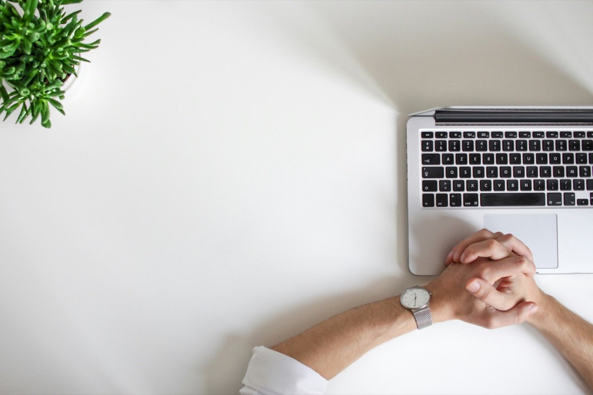 Hands folded beside a laptop on a white desk