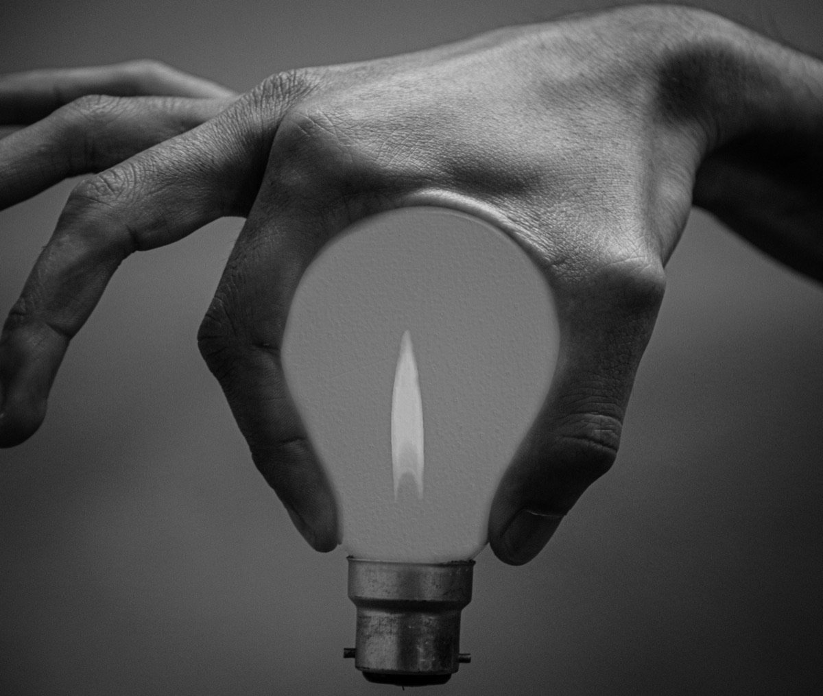 A hand holding a light bulb with a flame burning inside it
